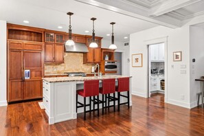 Une cuisine avec des meubles en bois, un îlot central doté de tabourets et des luminaires suspendus.