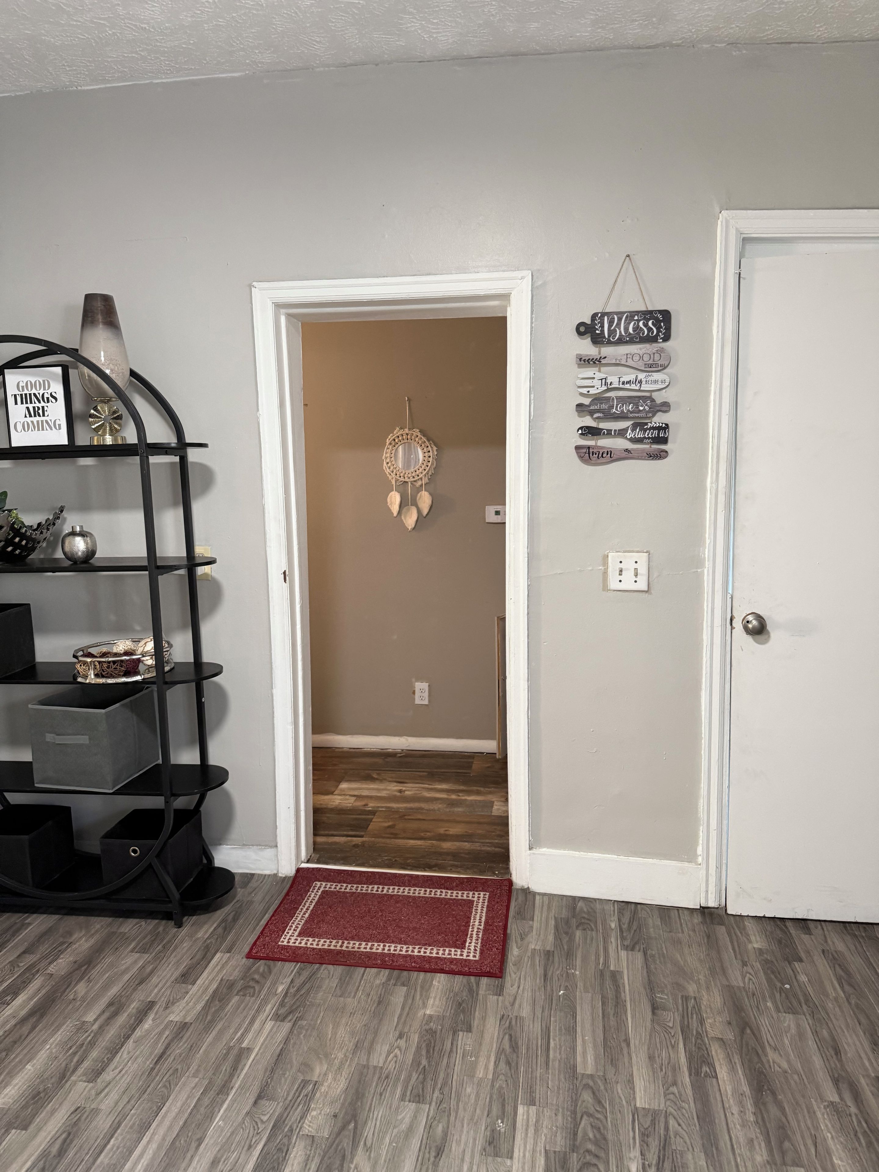A hallway with a black metal shelf unit, a red rug, and a door with a wall-mounted sign.