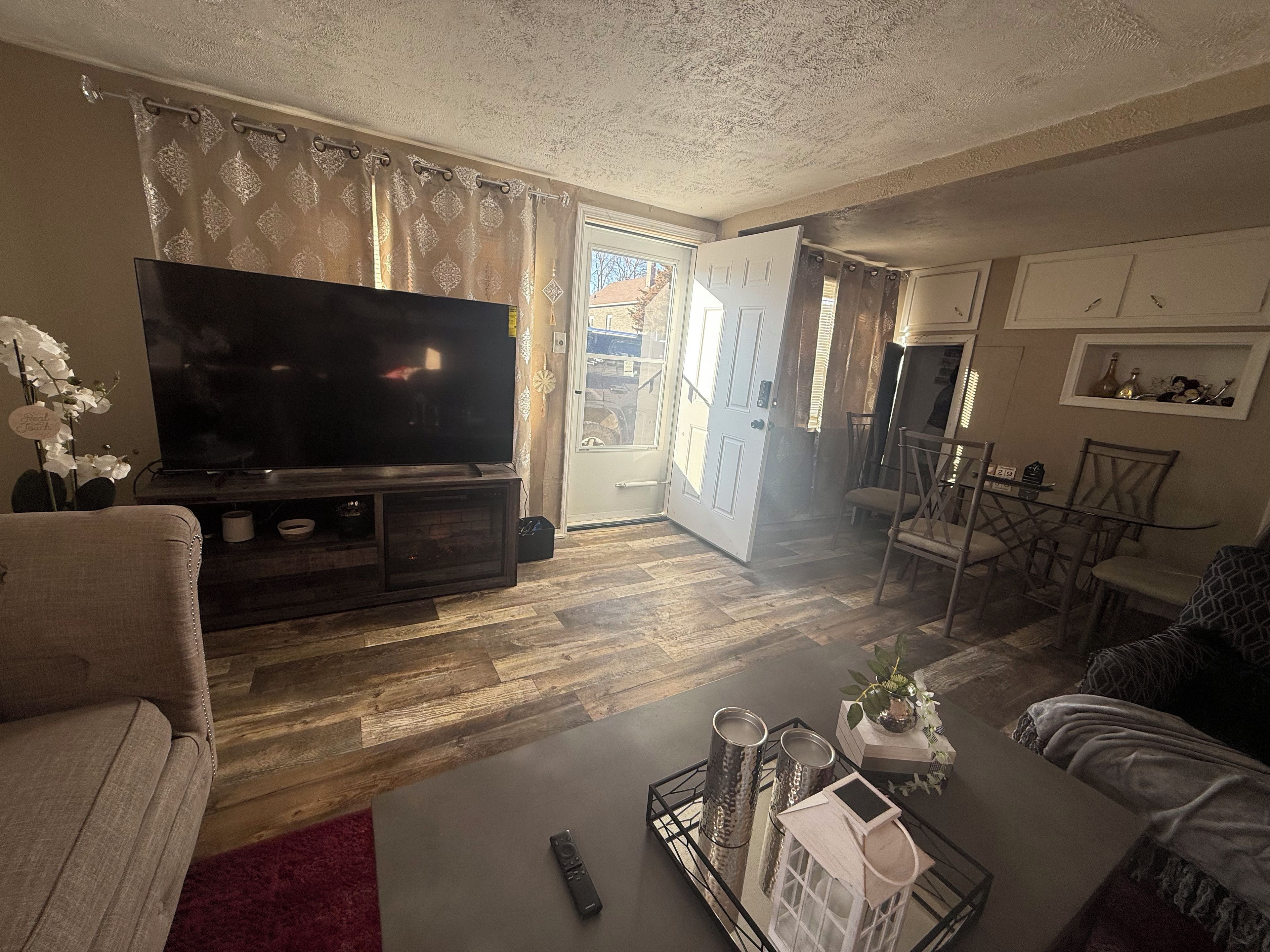 Una sala de estar con televisor de pantalla plana, una mesa de centro con objetos decorativos y un comedor con sillas y una mesa.