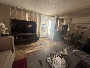 Ein Wohnzimmer mit Flachbildfernseher, einem Couchtisch mit Dekoration und einem Essbereich mit Stühlen und Tisch.