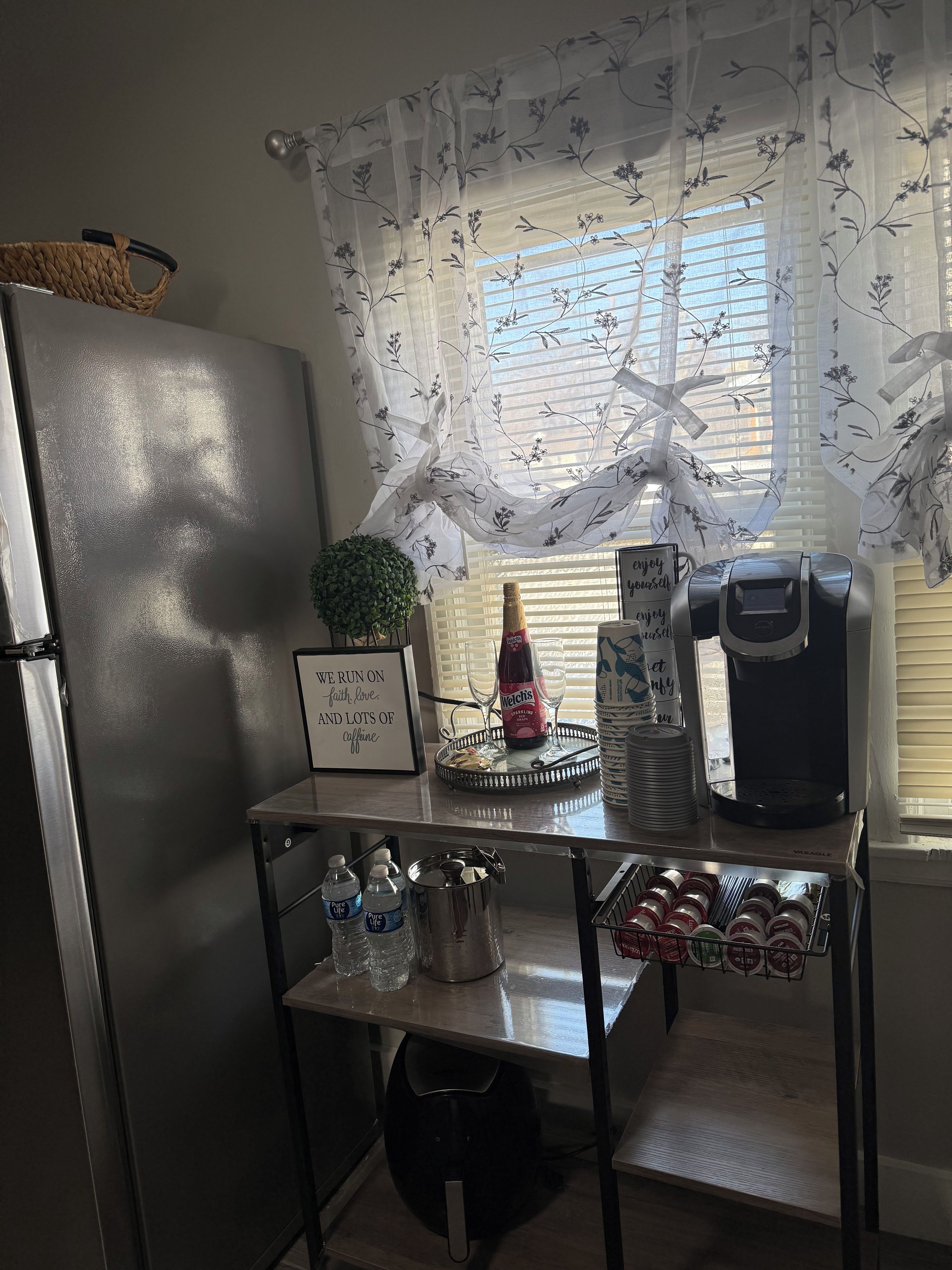 A kitchen counter with a refrigerator, a coffee maker, a bottle of Welch's, a tray with a glass, and a sign with a motivational quote.