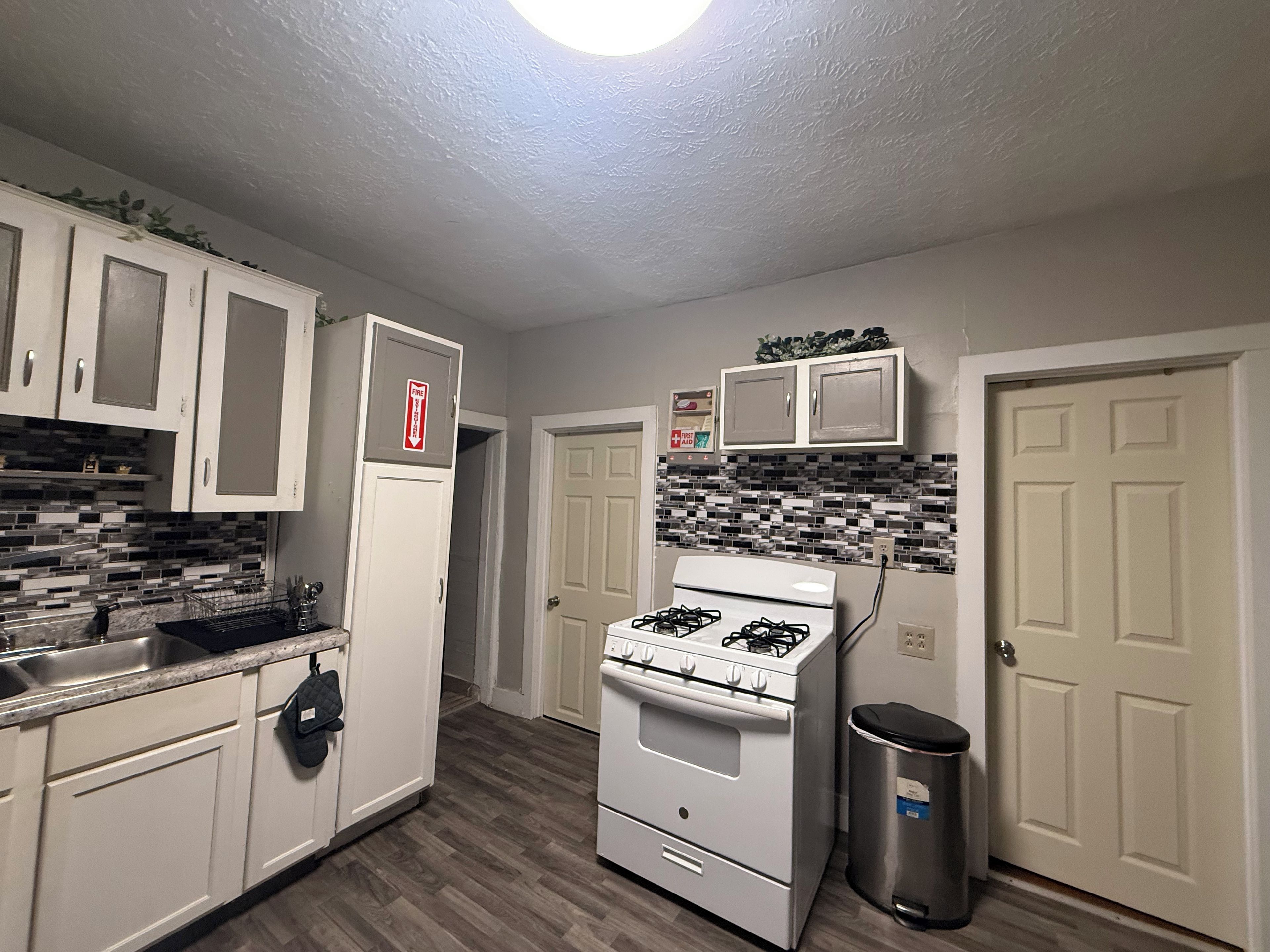 A kitchen with white cabinets, a gas stove, a trash can, and a fire extinguisher.