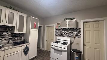 A kitchen with white cabinets, a gas stove, a trash can, and a fire extinguisher.