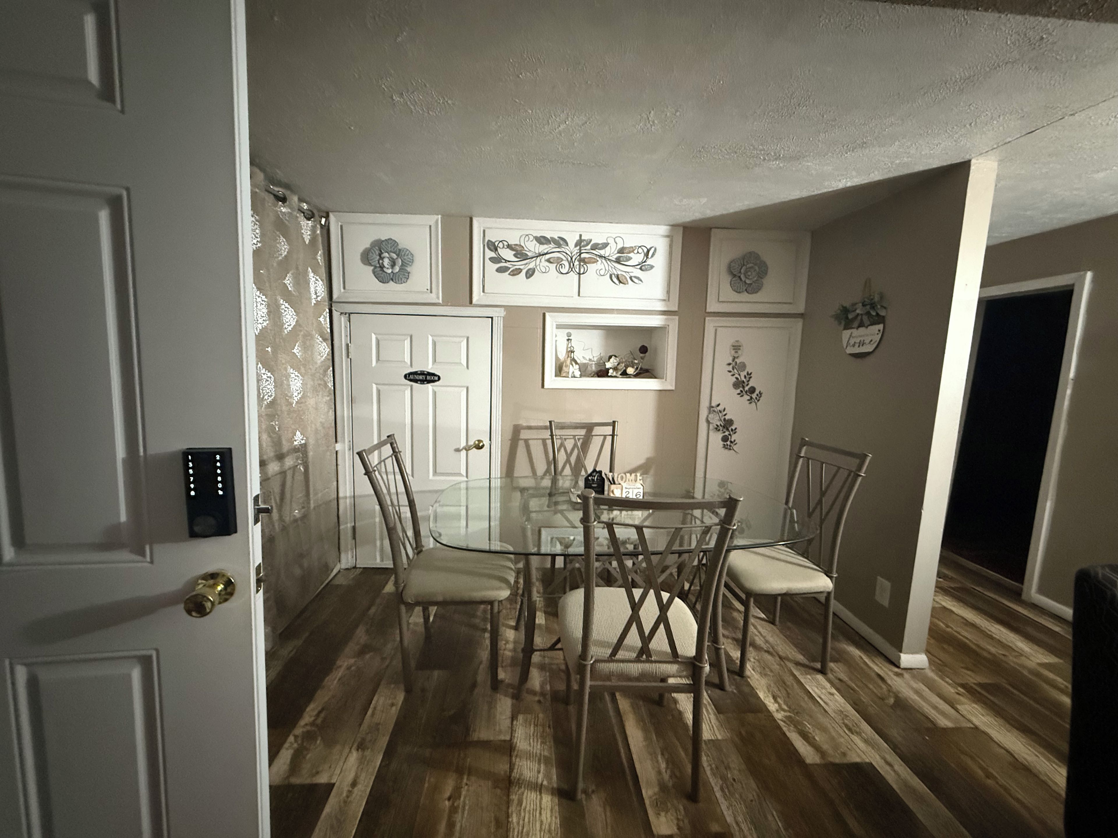 A dining area with a glass table surrounded by chairs, a door with a lock, and decorative wall art.