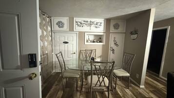 A dining area with a glass table surrounded by chairs, a door with a lock, and decorative wall art.