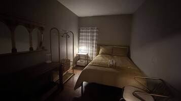 A dimly lit bedroom with a bed, a chair, a mirror, and a nightstand.