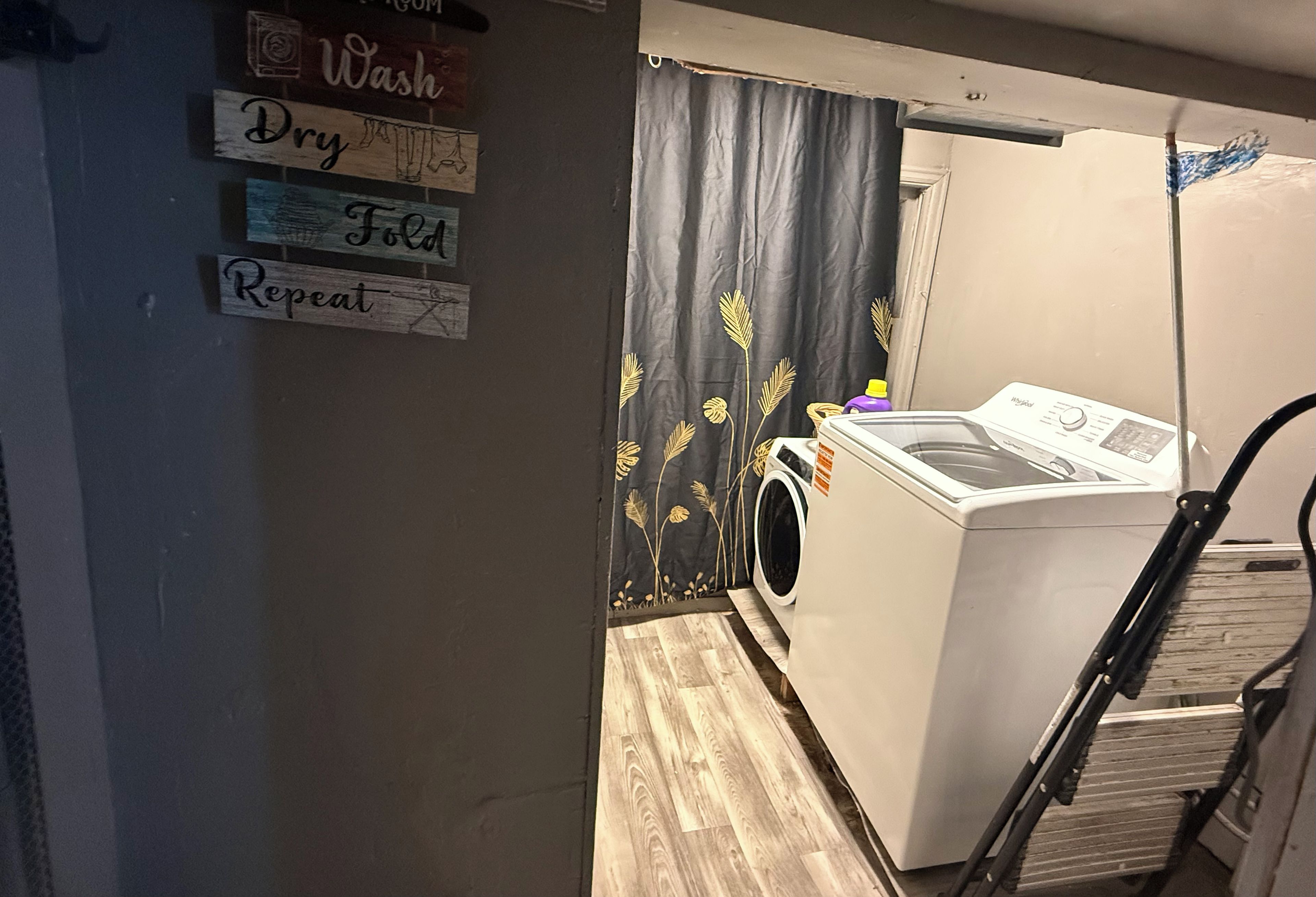 A laundry room with a washing machine, a drying rack, and a curtain with a leaf pattern.