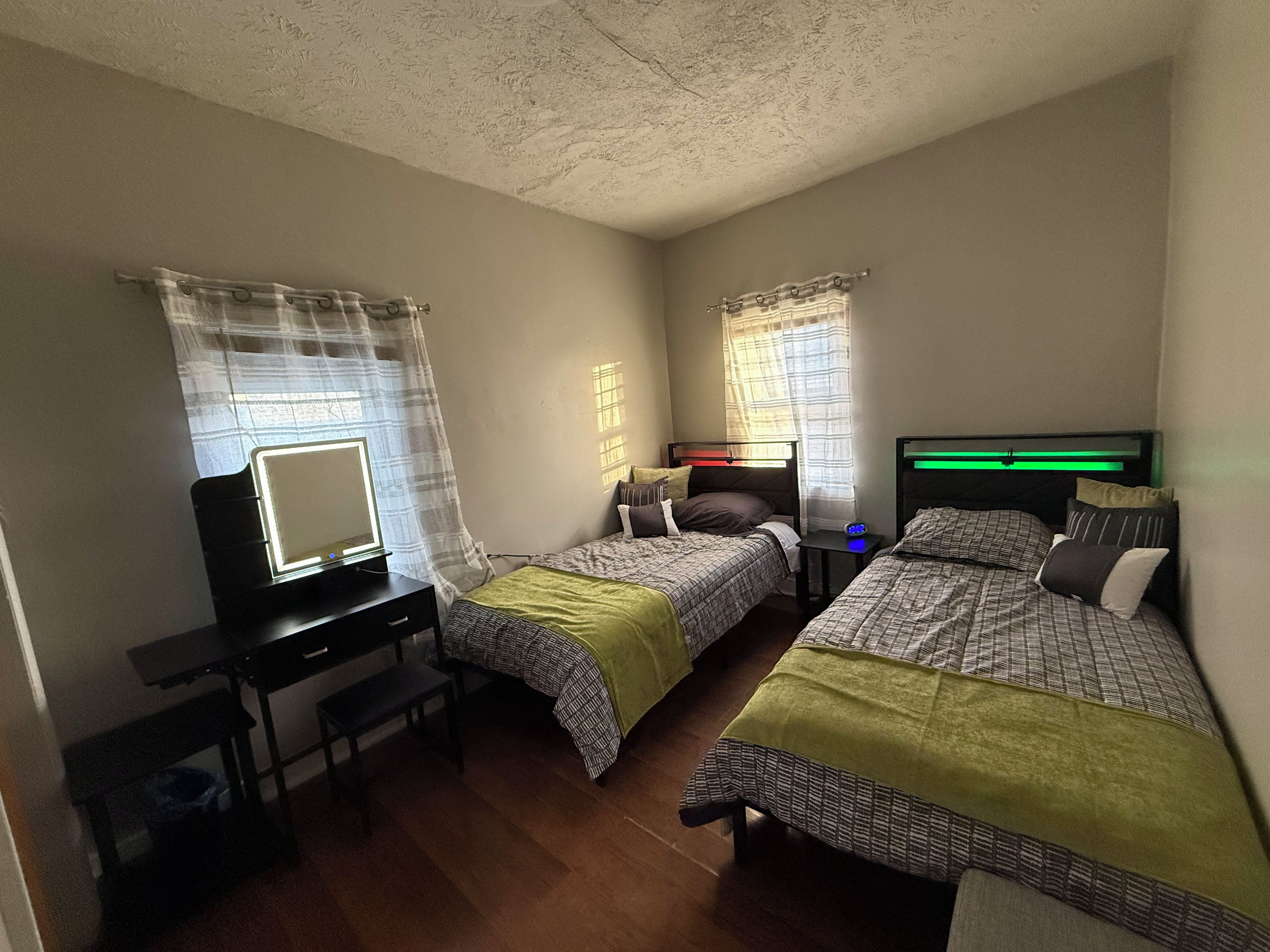 A bedroom with two beds, a desk, and a mirror.