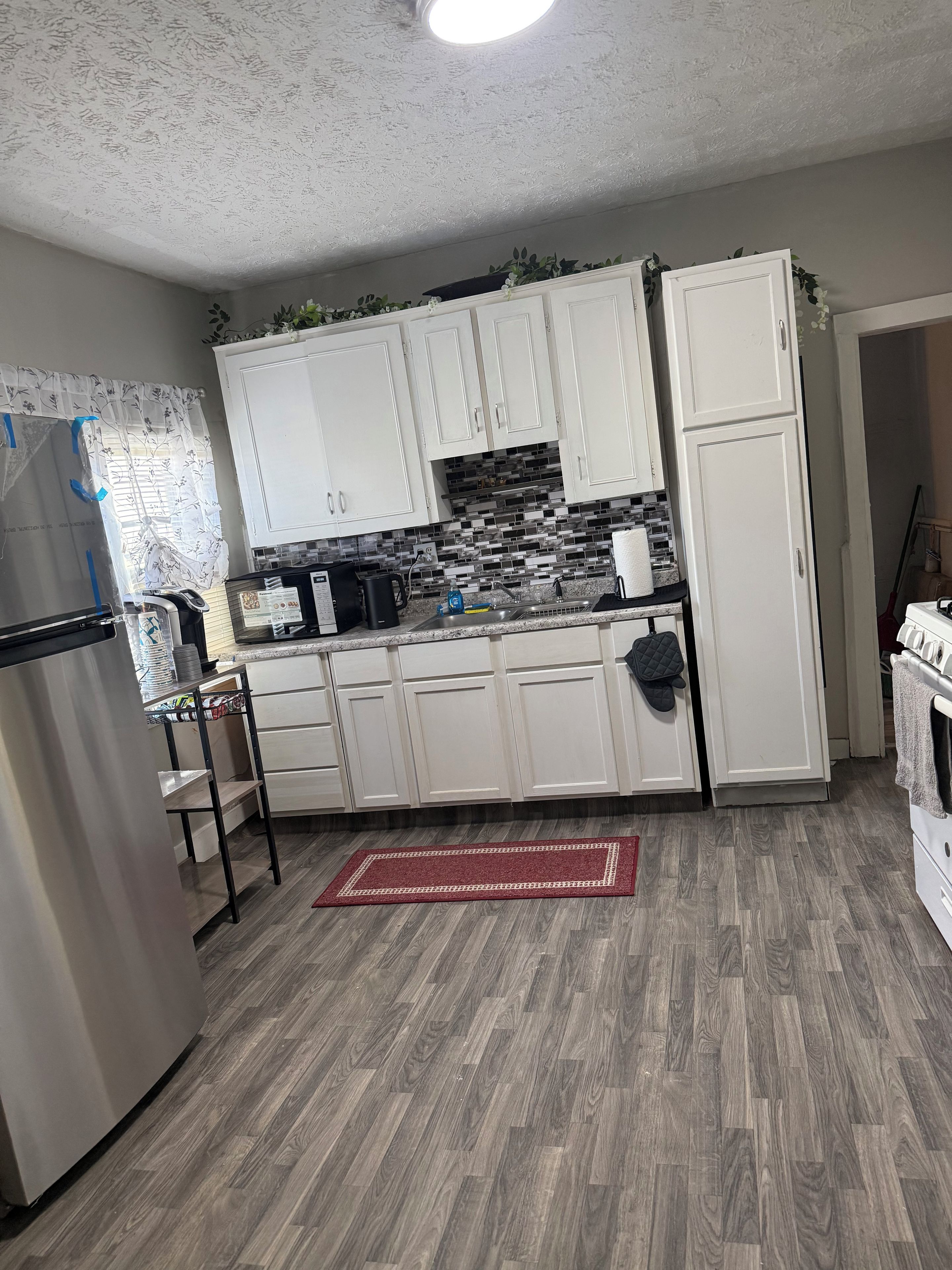 A kitchen with white cabinets, a stainless steel refrigerator, a tiled backsplash, and a red rug.