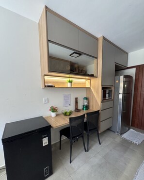 Cozinha compacta equipada com micro-ondas integrado, mini-refrigerador e área de refeições para duas pessoas.