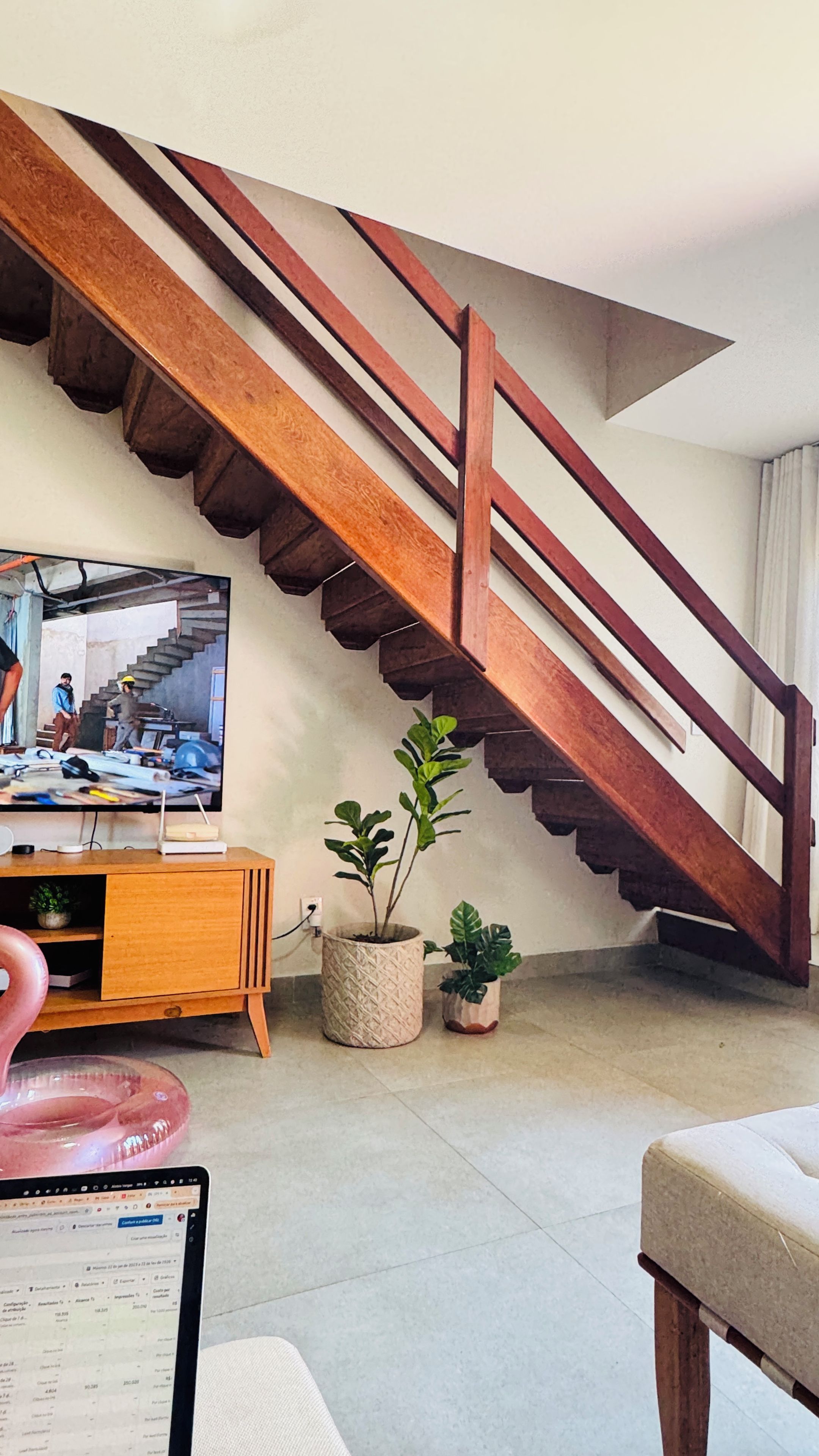 A staircase with wooden railings, a television on a wooden stand, and potted plants.
