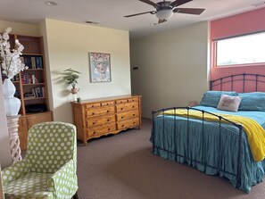Une chambre à coucher comprenant un lit, une commode, une chaise, une bibliothèque, un ventilateur de plafond et une fenêtre.