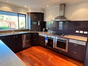 A modern kitchen with dark cabinetry, stainless steel appliances, and a large window. - Park Avenue Stay Close to Town (Takaka)