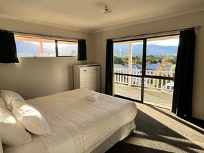 Un dormitorio con cama, cómoda y vistas a un lago y montañas a través de amplios ventanales.