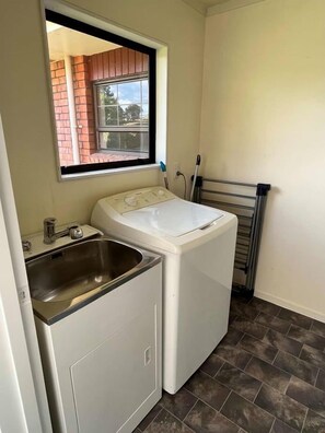 A compact laundry room with a washing machine, a sink, and a window. - Park Avenue Stay Close to Town (Takaka)