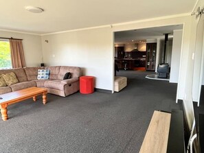 A living room with a sofa, a coffee table, and a red ottoman. There is a kitchen visible through an open doorway. - Park Avenue Stay Close to Town (Takaka)