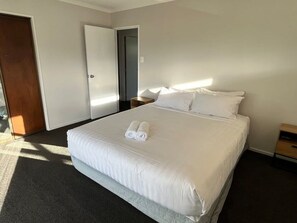 A hotel room with a large bed, a bedside table, a nightstand, and a door. - Park Avenue Stay Close to Town (Takaka)