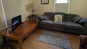 Un salon avec une table basse en bois, un canapé gris, un tapis à motifs et une lampe fixée au mur.