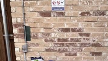 A brick wall with a pool rules sign and two wicker baskets containing beach balls and a red towel.