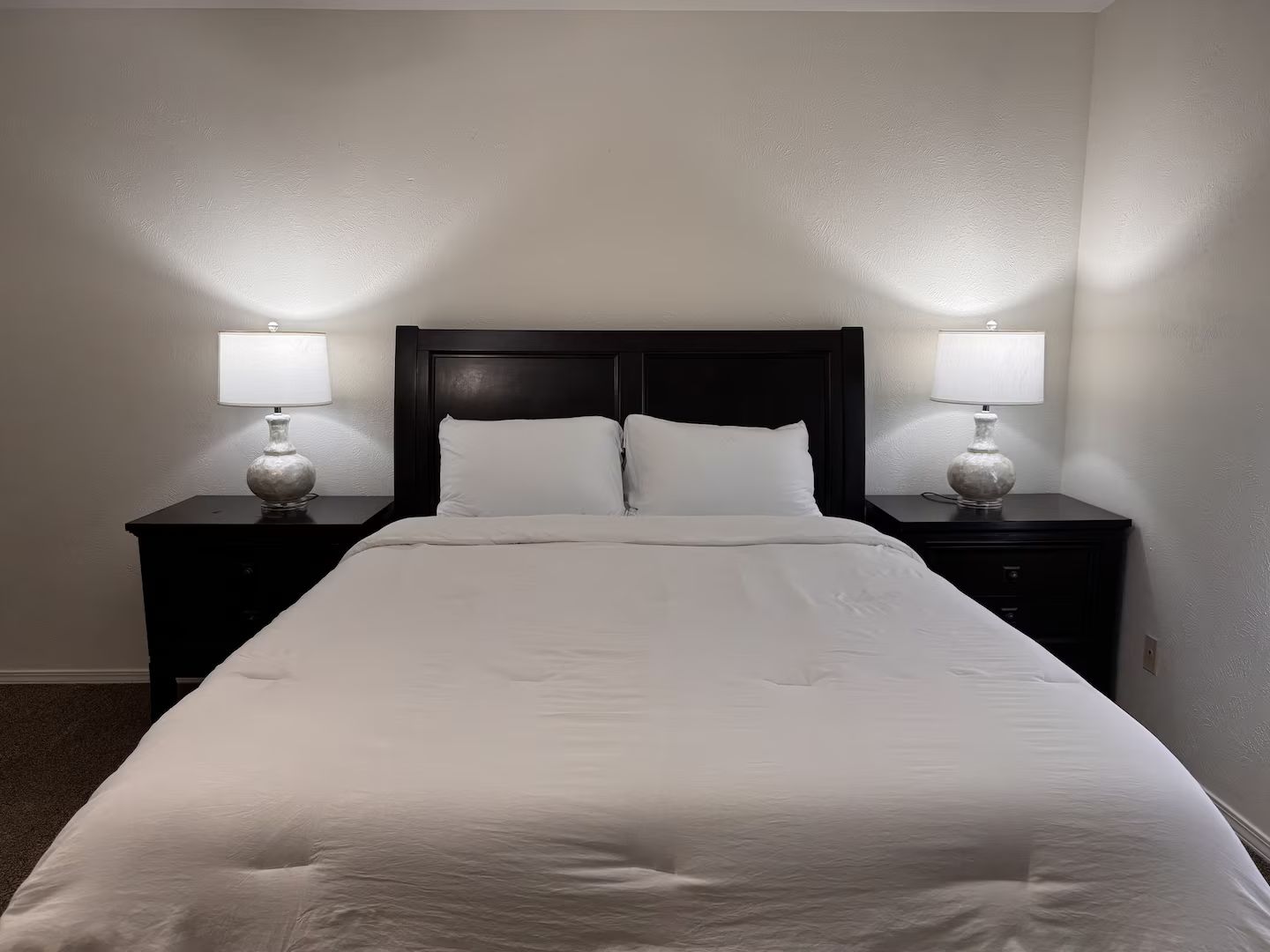 A hotel room with a large bed, two bedside tables with lamps, and a dark headboard.