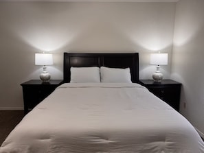 A hotel room with a large bed, two bedside tables with lamps, and a dark headboard.