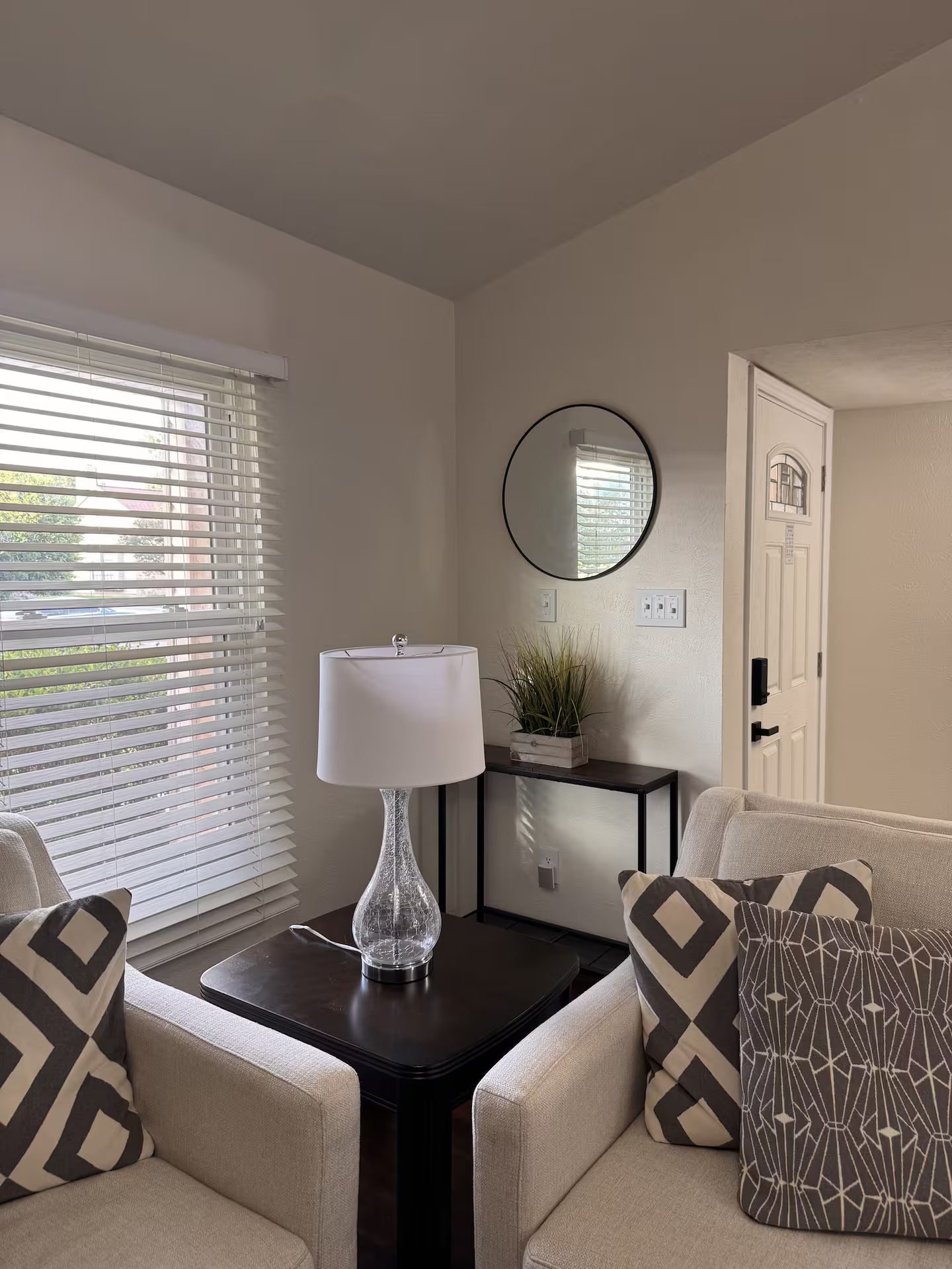 A room with a sofa, a table with a lamp, a mirror, and a door.