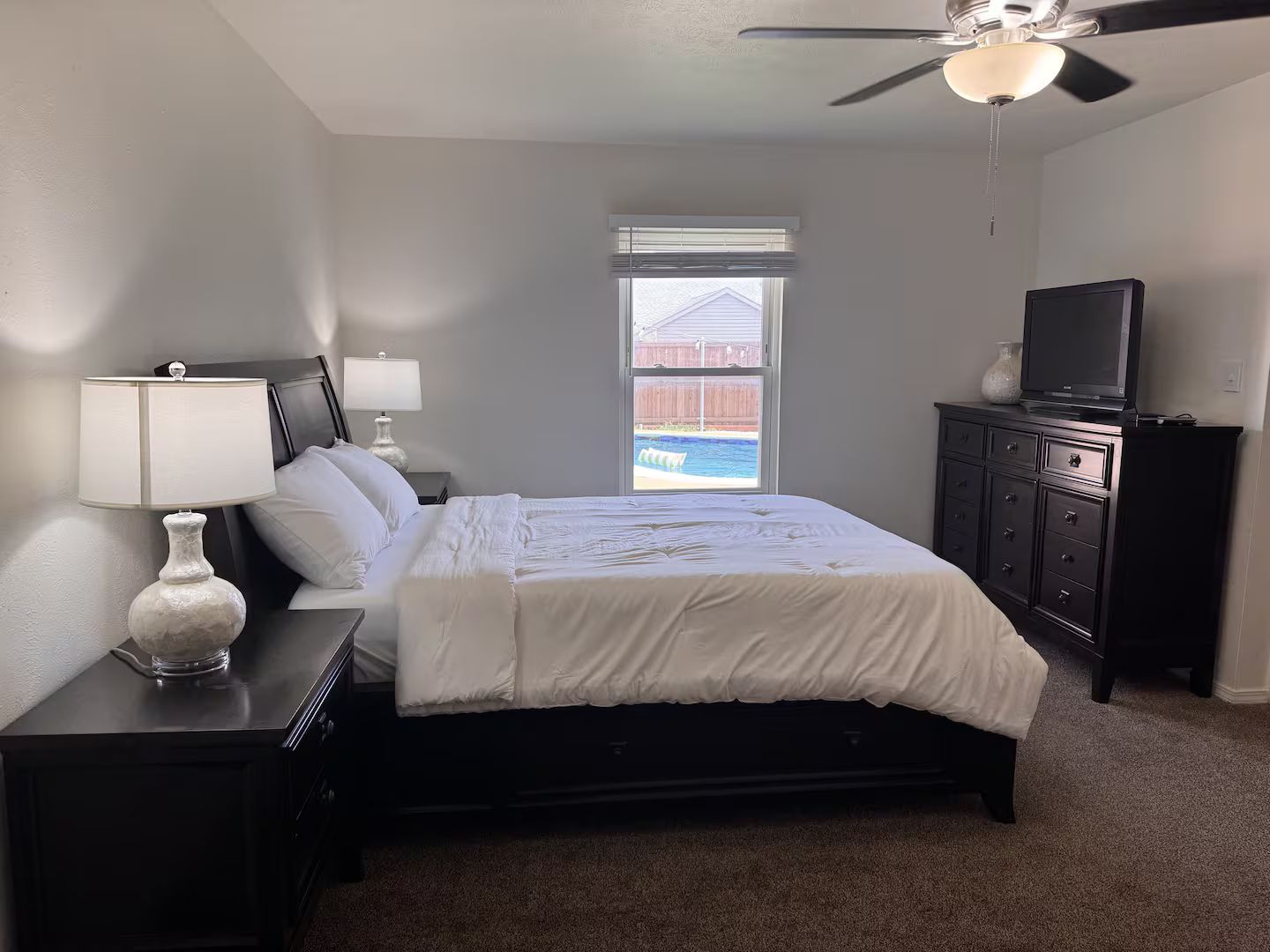 A bedroom with a bed, nightstands, a dresser, a television, and a ceiling fan.