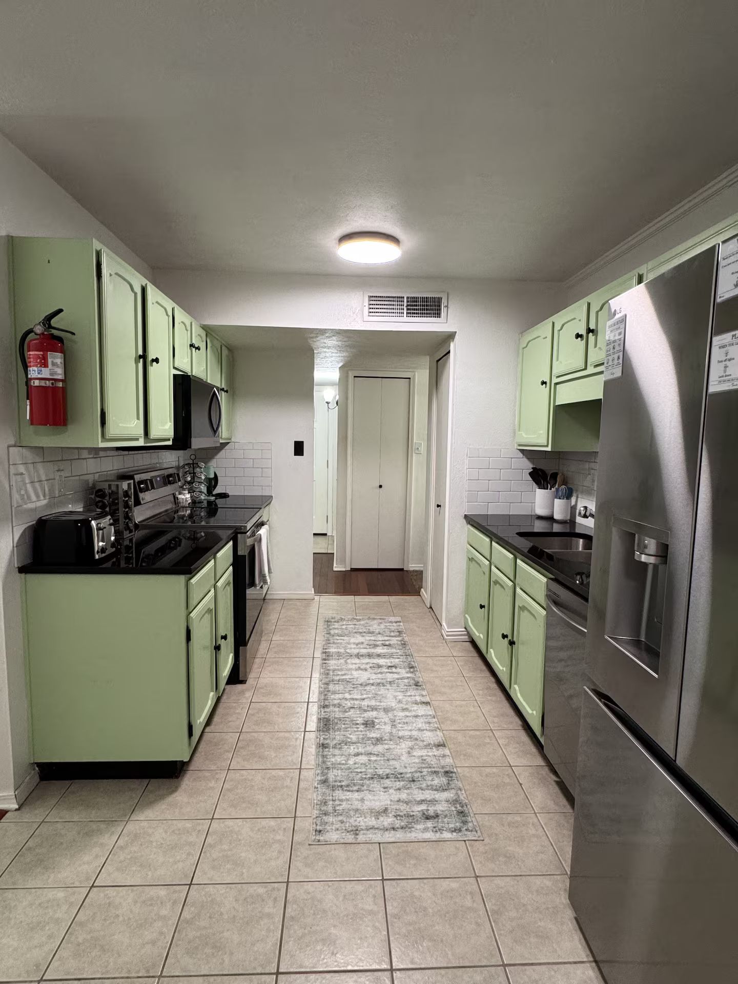 A kitchen with green cabinets, a stainless steel refrigerator, and a tiled floor.