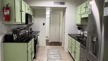 A kitchen with green cabinets, a stainless steel refrigerator, and a tiled floor.