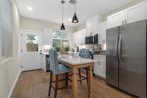 A modern kitchen with white cabinetry, a stainless steel refrigerator, and a dining area with a wooden table and chairs. - Modern 3BR Houston Retreat Stylish & Spacious (Houston)