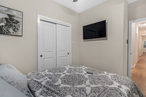 A bedroom with a bed, a wardrobe, a television, and a hallway leading to another room. - Modern 3BR Houston Retreat Stylish & Spacious (Houston)