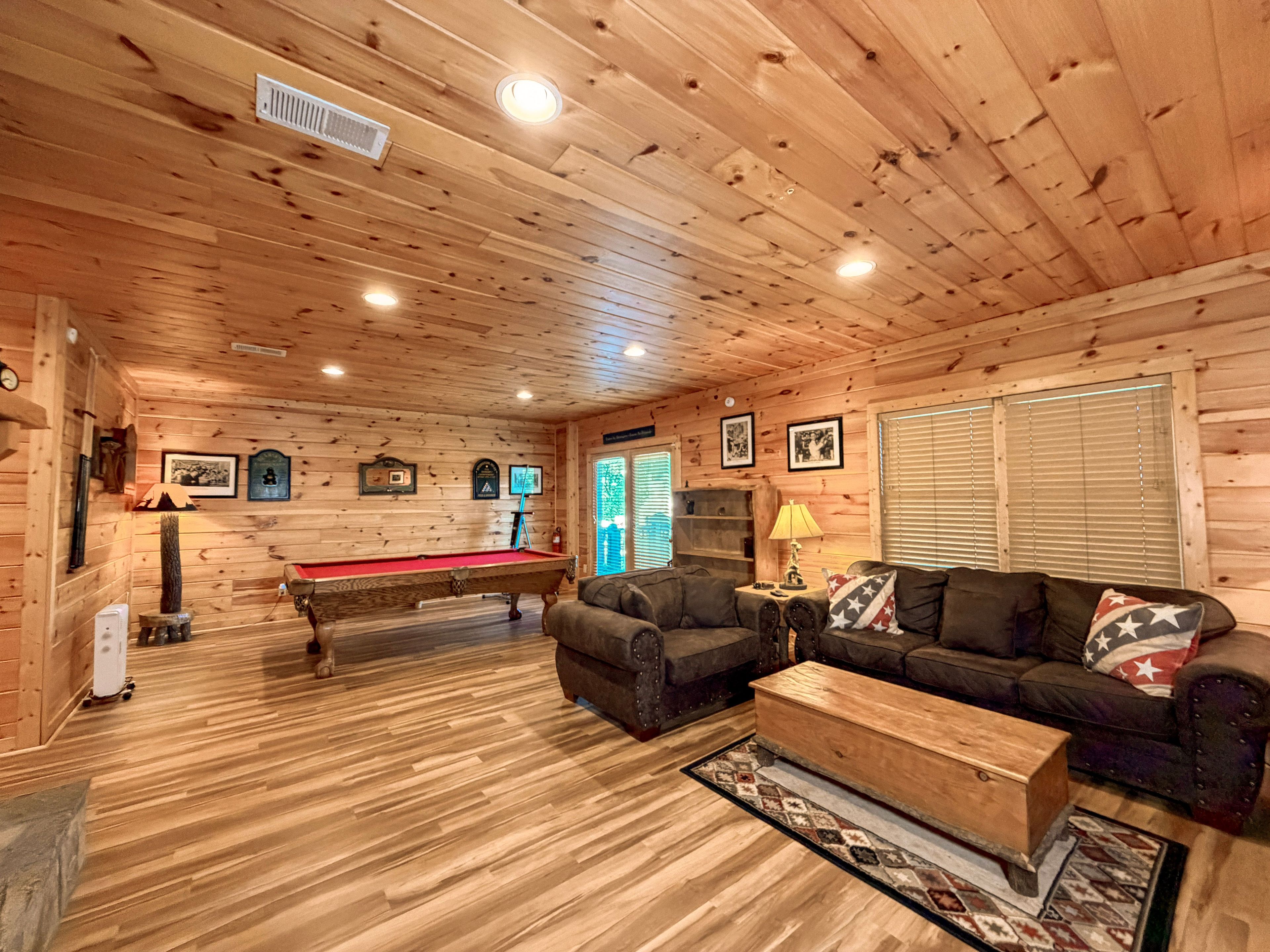 A wooden interior with a pool table, sofa, and a fireplace.