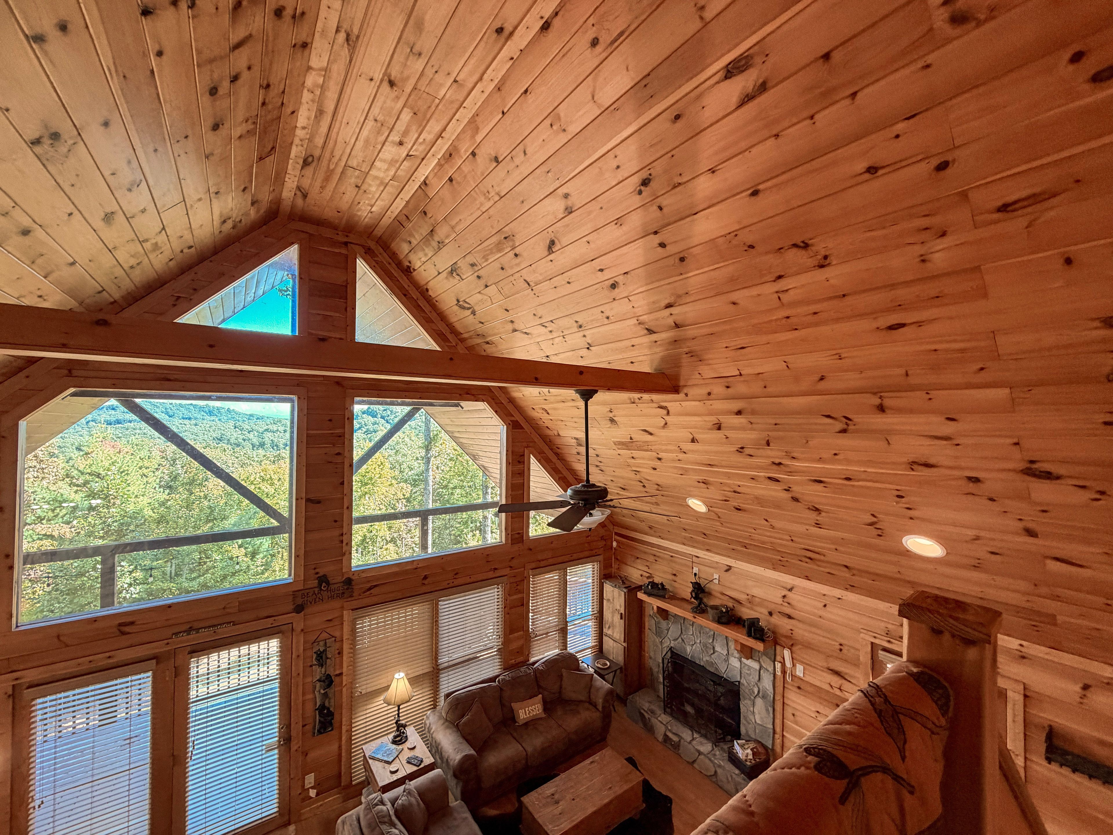 A cabin with a stone fireplace, wooden ceiling beams, and large windows offering a view of the forest.