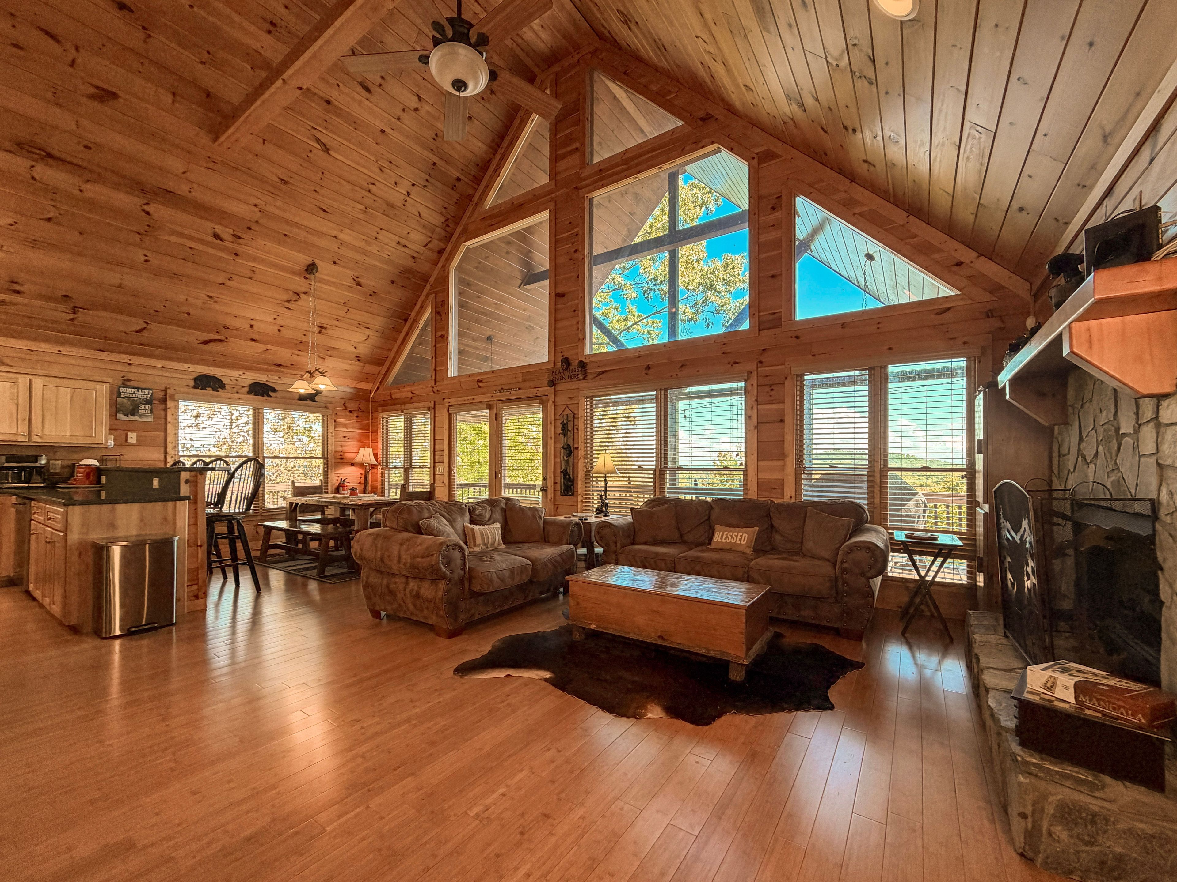 A spacious living area with a high ceiling, wooden beams, a fireplace, and large windows.
