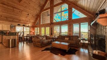 A spacious living area with a high ceiling, wooden beams, a fireplace, and large windows.