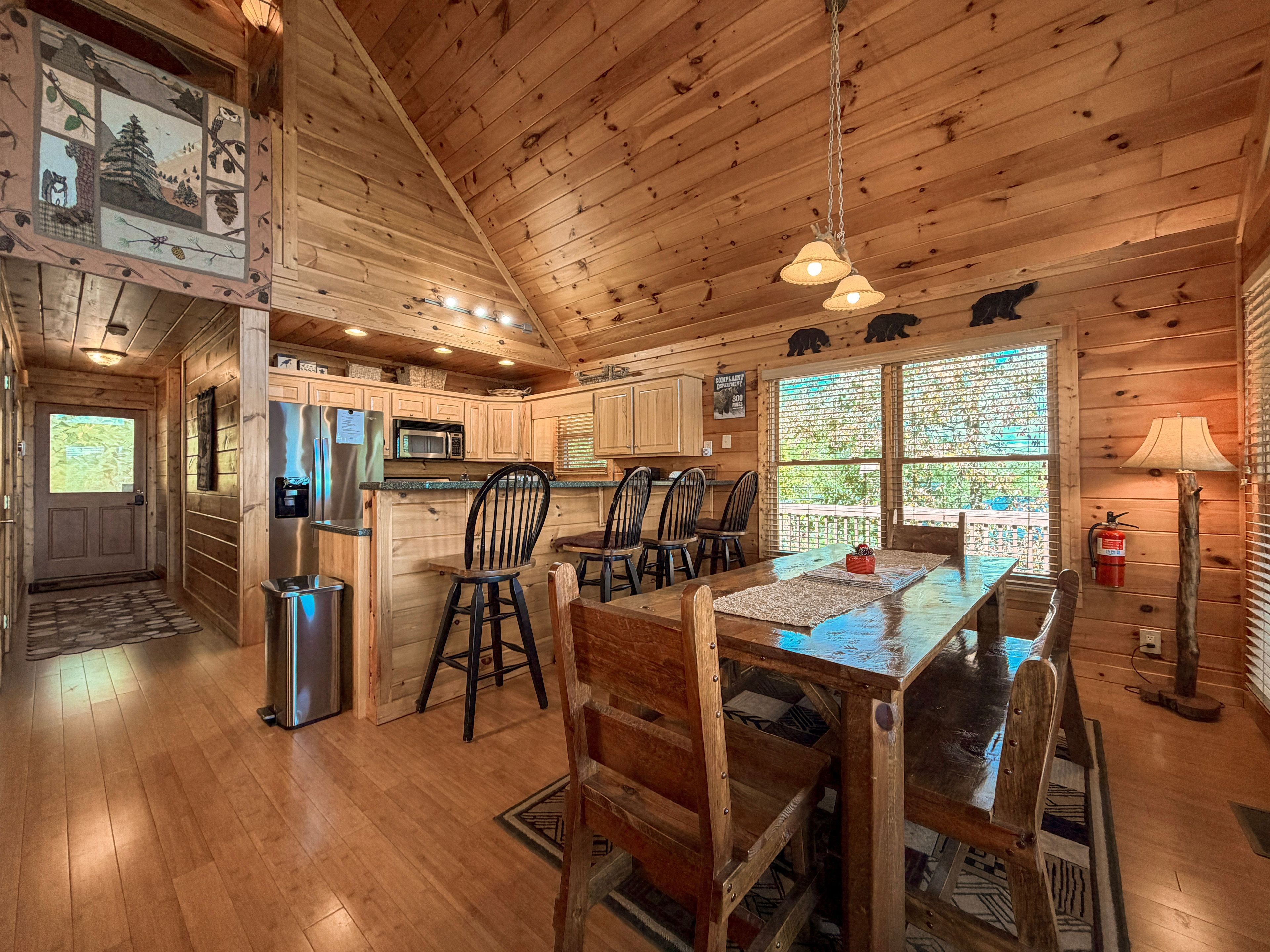A wooden cabin interior with a kitchen, dining area, and a large window.