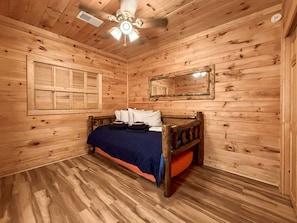 A wooden cabin room with a bed, a ceiling fan, and a window with shutters. - Mountain View Cabin Near Downtown Blue Ridge (Blue Ridge)