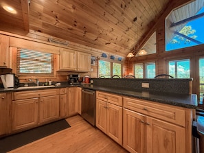 A wooden cabin kitchen with a granite countertop, wooden cabinets, and a large window with a view of trees. - Mountain View Cabin Near Downtown Blue Ridge (Blue Ridge)