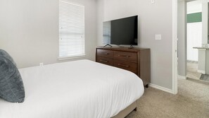 Ein Schlafzimmer mit einem Bett, einer Kommode, einem Fernseher und einer Tür zu einem anderen Raum.
