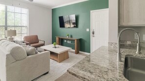 Ein modernes Wohnzimmer mit einer Couch, einem Couchtisch und einem an einer grünen Wand montierten Fernseher.