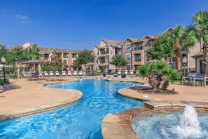 A swimming pool with lounge chairs and a fountain, surrounded by multi-story buildings with balconies. - Landing | Stylish 2BD, Clubhouse, Gym (Katy)