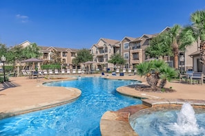 A swimming pool with lounge chairs and a fountain, surrounded by multi-story buildings with balconies. - Landing | Amazing 1BD, Gym, Clubhouse (Katy)
