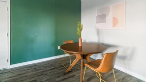Ein Konferenzraum mit einem runden Tisch, zwei Stühlen, einer Zimmerpflanze und einer Wand mit geometrischem Muster.
