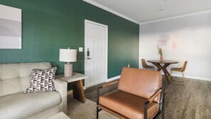 Ein Wohnzimmer mit einer Couch, einem Ledersessel, einem kleinen Tisch mit Lampe und einem Essbereich mit Stühlen und Tisch.
