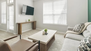 A living room with a sofa, coffee table, and a TV mounted on the wall. - Landing | Stunning 1BD, Gym, Clubhouse (Katy)