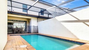 Una piscina con un solárium con baldosas, un cerramiento de vidrio y un patio amoblado.