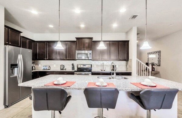 A modern kitchen with dark wood cabinets, stainless steel appliances, and a granite island with bar stools. - Vrbo Property (Four Corners)