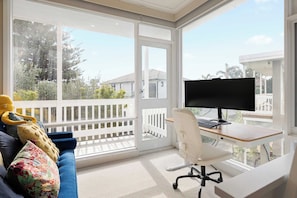 A sunlit room with a large window, a desk with a computer, and a sofa with decorative pillows. - Beachgate Aspendale Direct Beach Access (Aspendale)