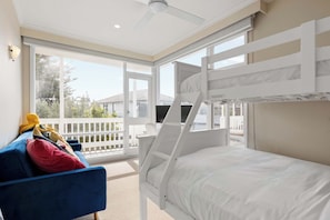 A room with bunk beds, a blue sofa, and a balcony with a view of houses. - Beachgate Aspendale Direct Beach Access (Aspendale)