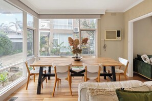 A dining area with a wooden table, white chairs, and a vase of flowers. - Beachgate Aspendale Direct Beach Access (Aspendale)